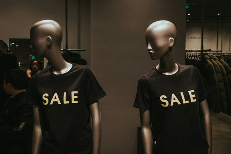 Store mannequins wearing black SALE t-shirts in a retail clothing shop display