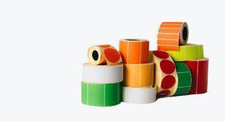Assorted colored thermal transfer label rolls stacked on a white background.